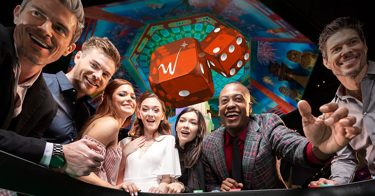 A group of five people laughing and celebrating around a craps table with two large orange dice mid-air.
