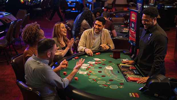 A group of friends smiling and laughing while playing blackjack at a casino table.